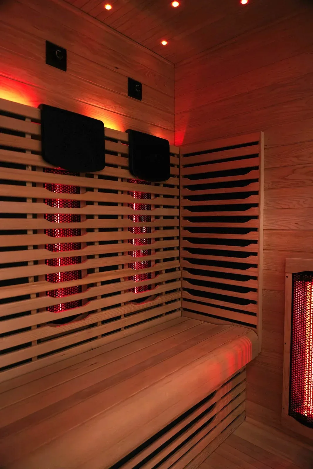 Infrared sauna cabin with dark square panels on the back wall and a glowing red heater at the side