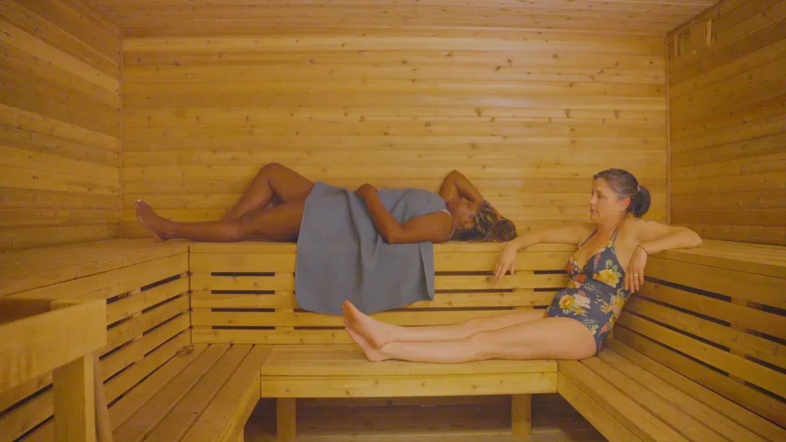 Two people relaxing on the upper and lower wooden benches of a sauna