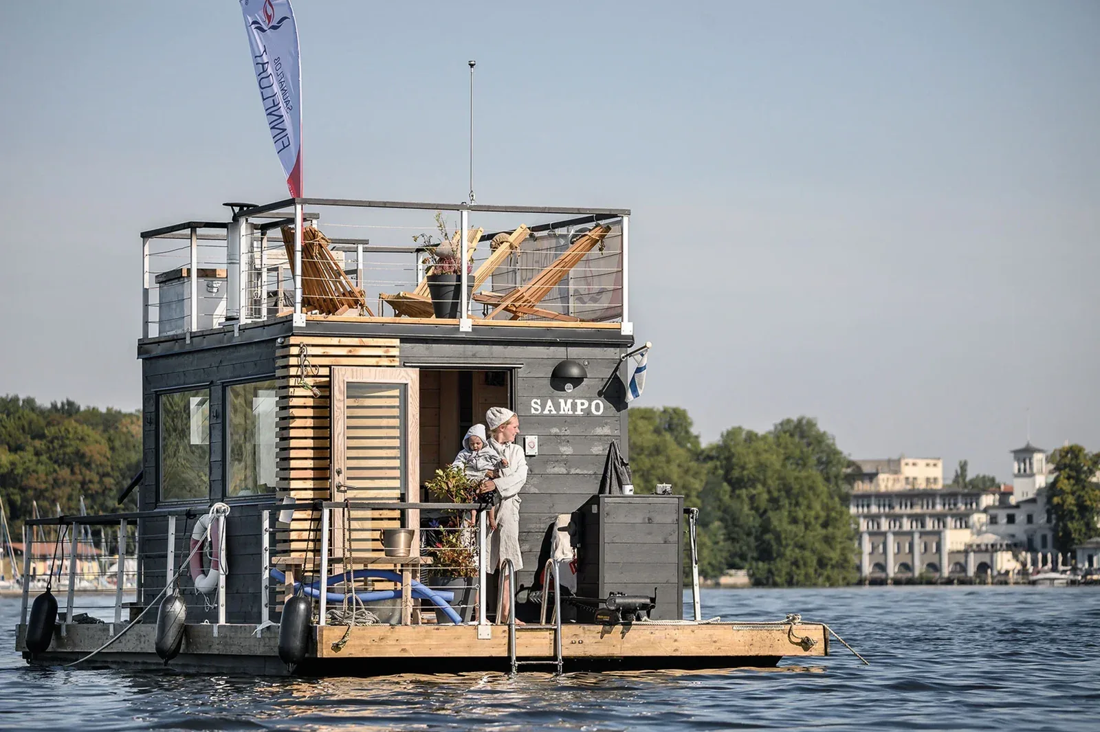 A two-storey floating sauna boat with a roof terrace on a lake