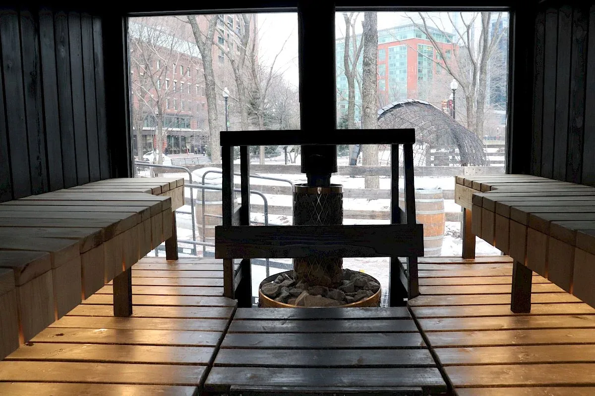 Sauna with slatted benches either side of a stove surrounded by a wooden rail, with a window behind