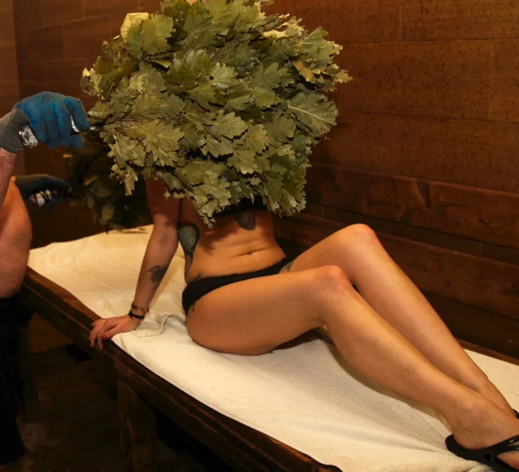 Bath attendant whisking a woman with a large leafy broom