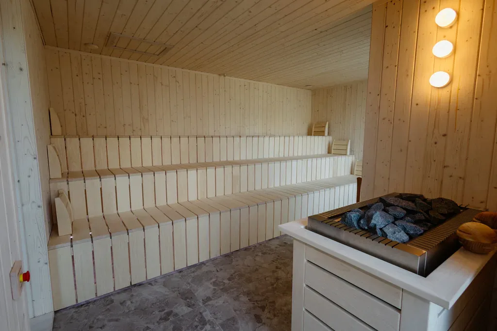 Bright wooden sauna with tiered benches and a heater full of stones