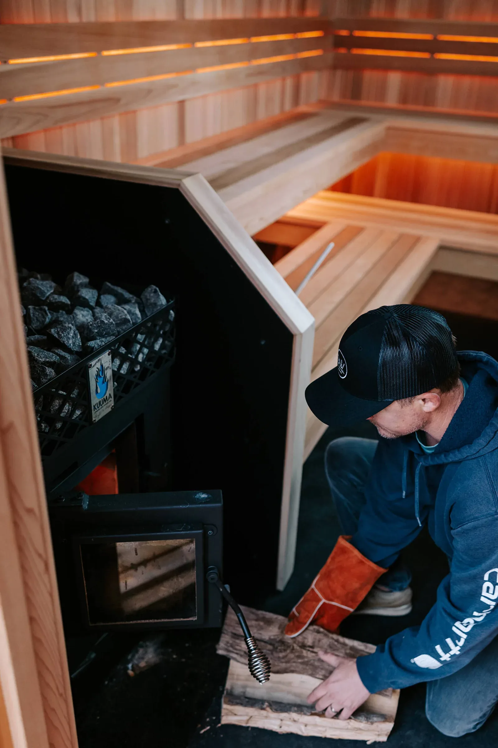 Man in a heat-proof glove putting firewood into a sauna stove