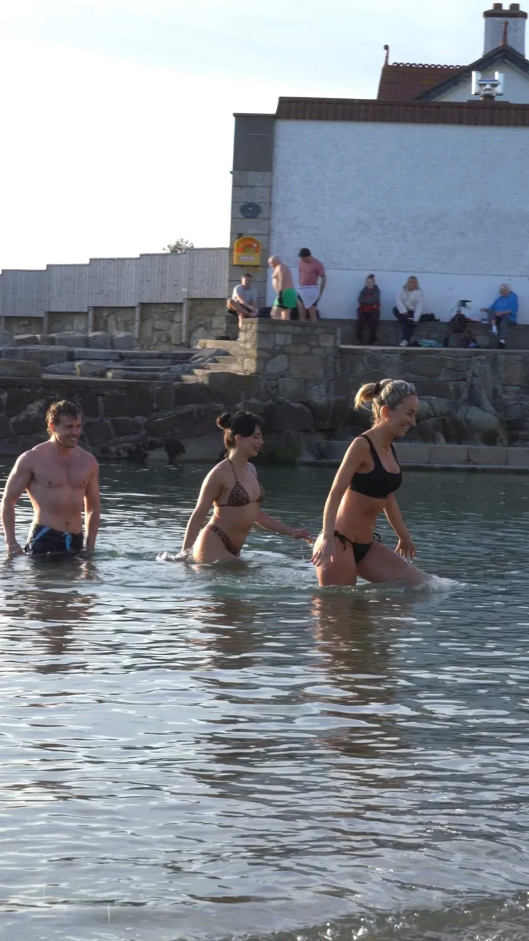People wading into the sea next to a seaside sauna