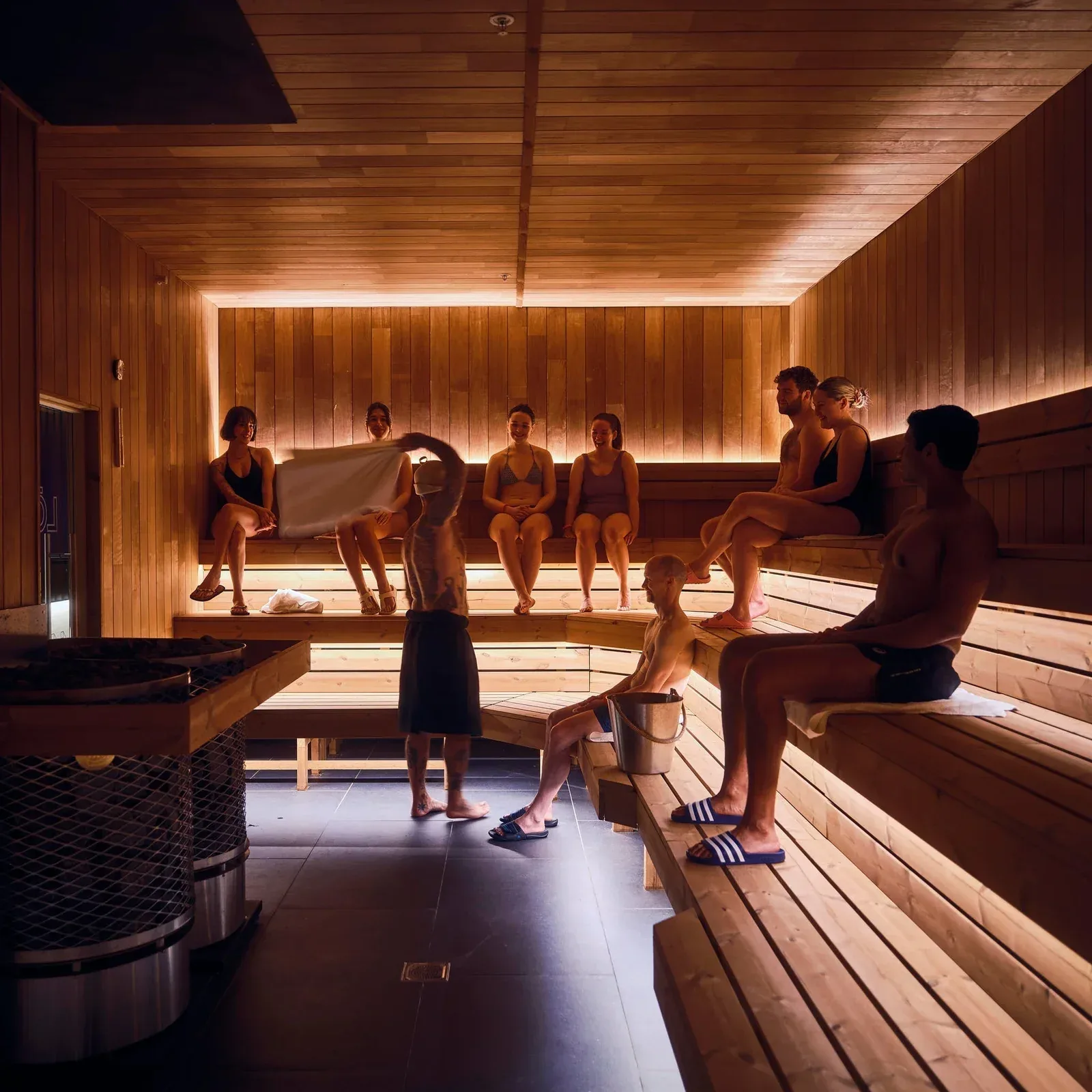 People sitting on wooden benches in a busy public sauna