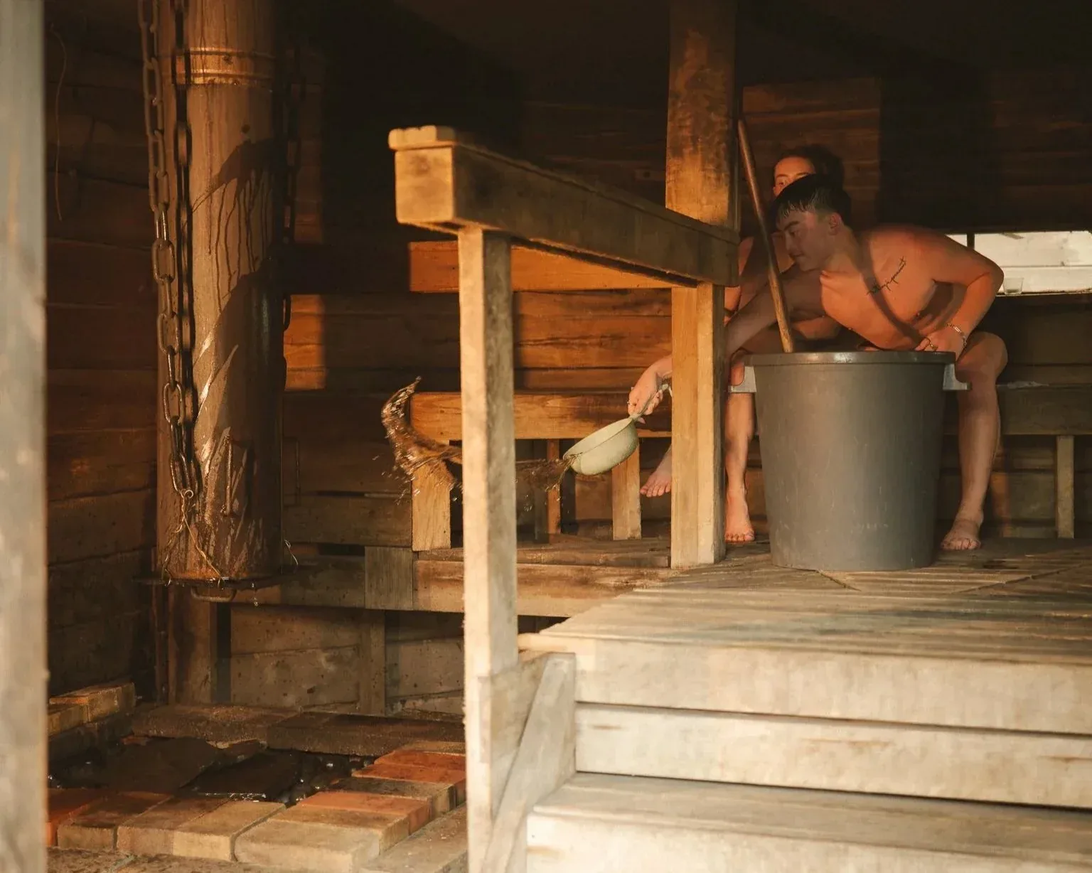 Man on a wooden sauna bench leaning over a large bucket