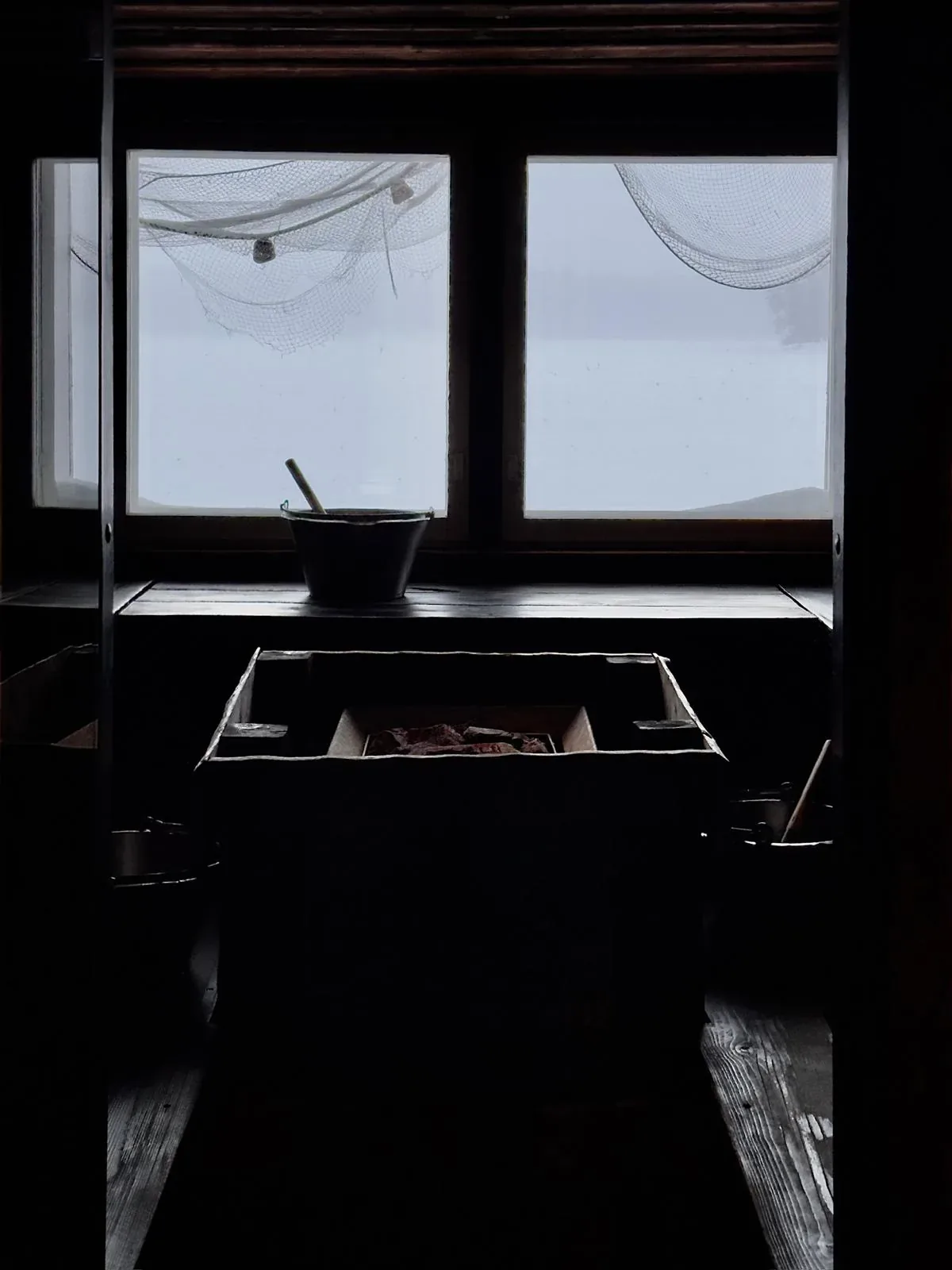 Dark sauna interior with a heater and a pot on top, below a window with pale light outside