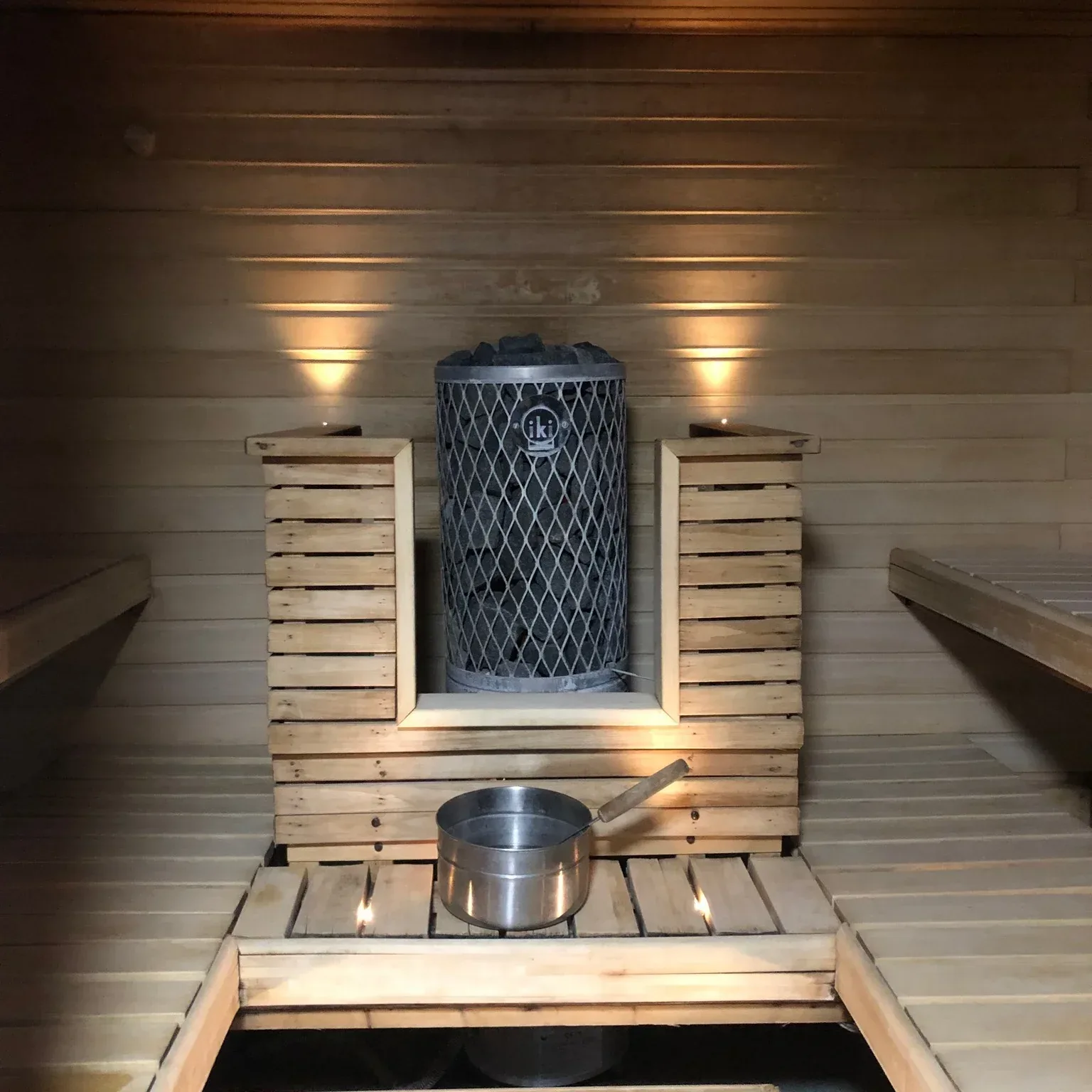 Sauna heater in a wooden surround with a metal water bucket in front