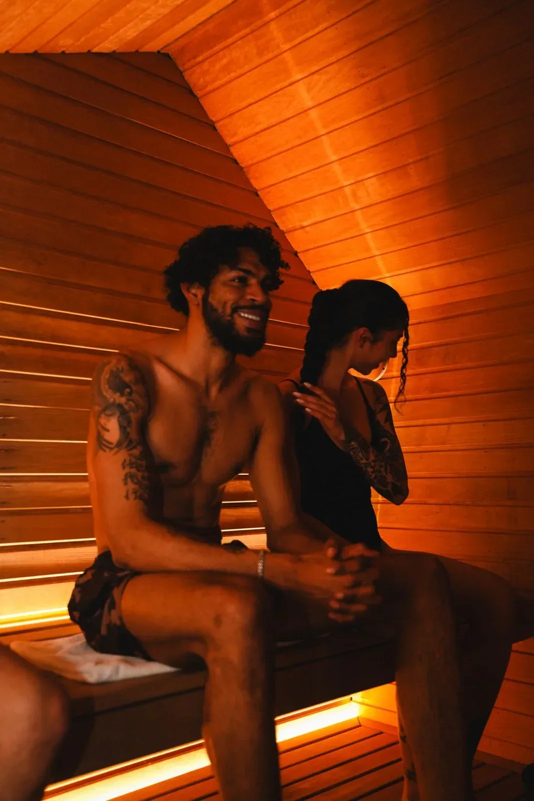 Man and woman sitting together on a sauna bench in warm orange light