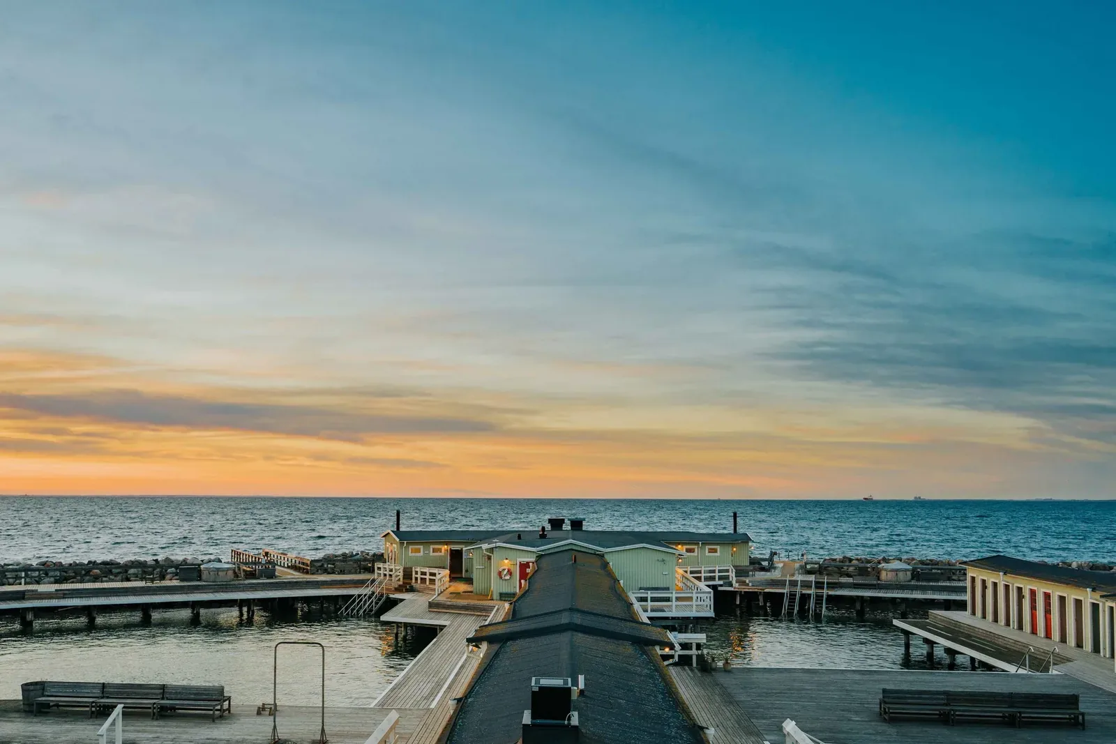 Wooden bathing house at the end of a long pier over the sea at sunset