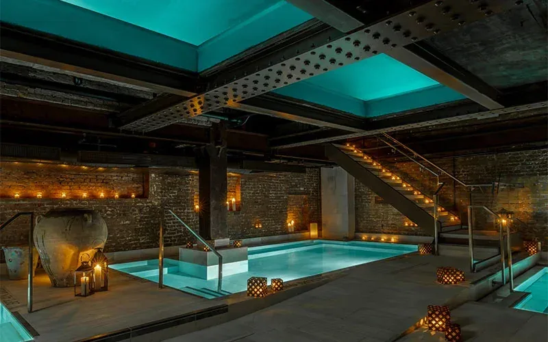 Candlelit underground bathhouse with several pools and brick walls