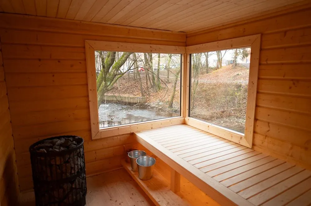 Wooden sauna bench under a large corner window looking out on trees