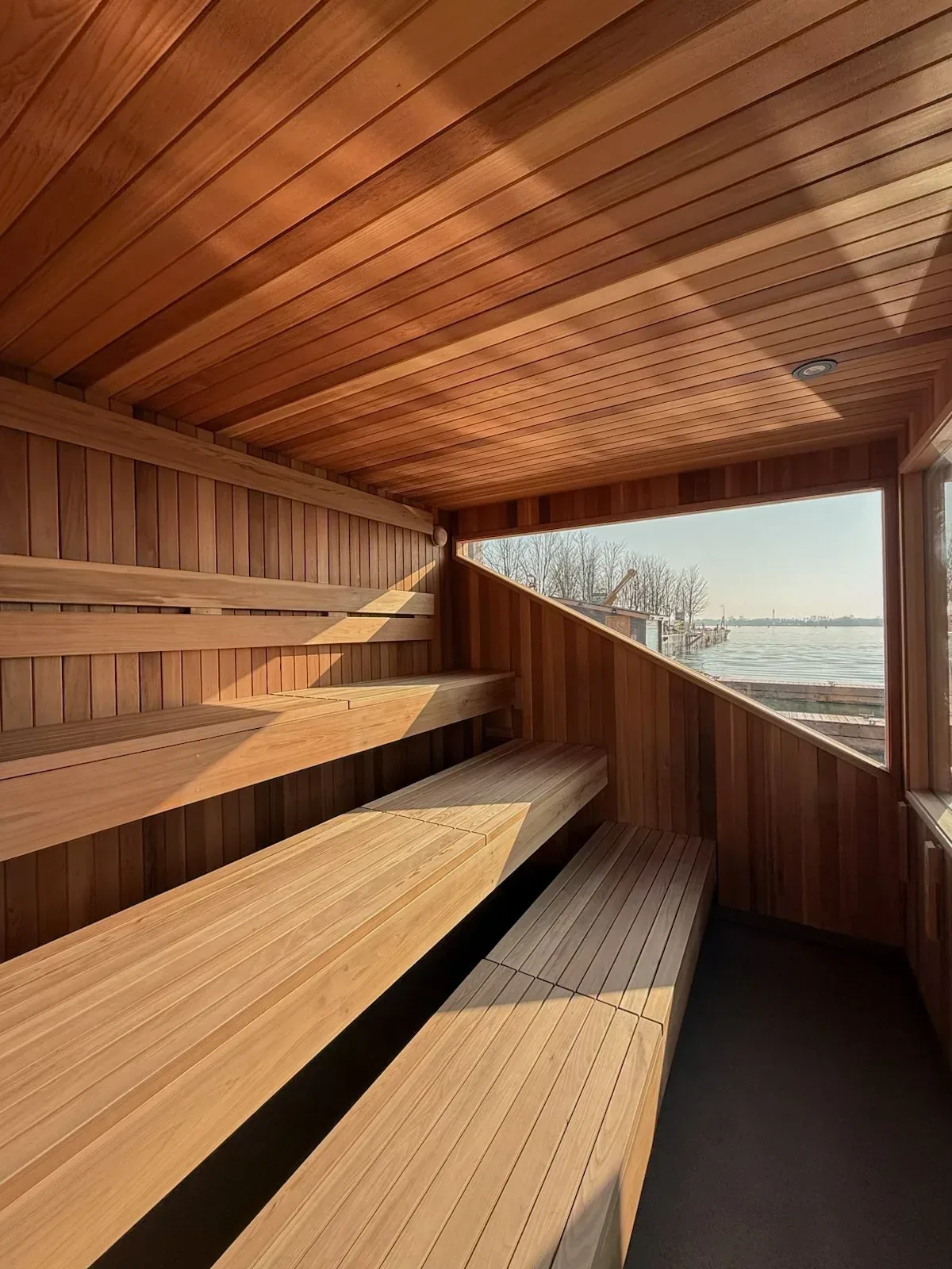 Inside a wooden sauna with benches facing a window onto the water
