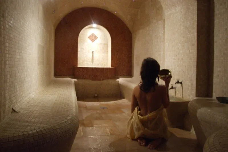 Woman sitting by a stone basin in a candle-lit hammam