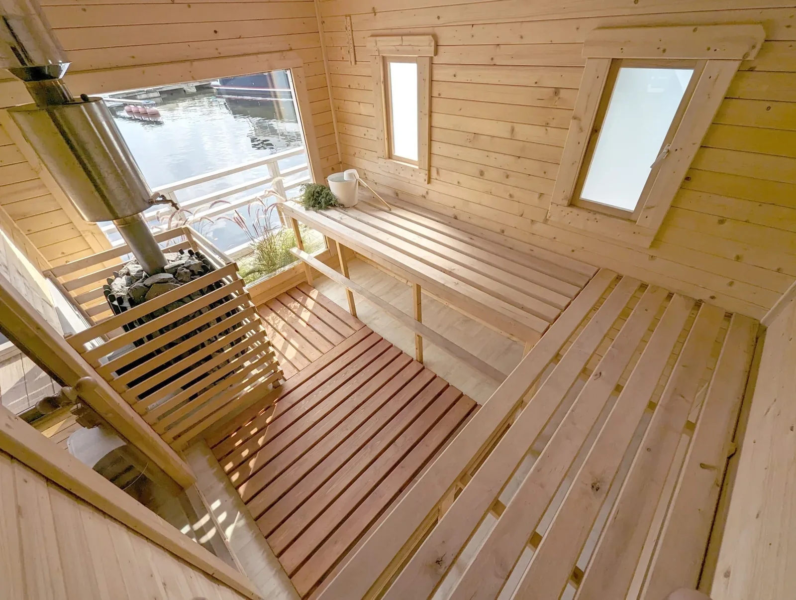 Bright wooden sauna interior with a heater and windows looking out onto water