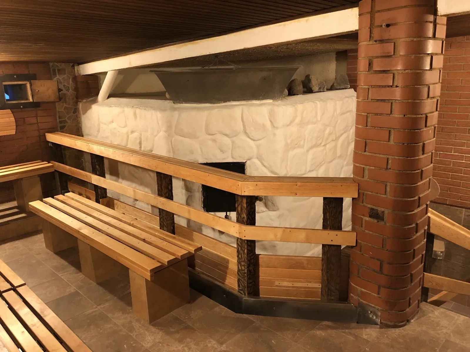 Wooden benches beside a large white stove set into a brick chimney