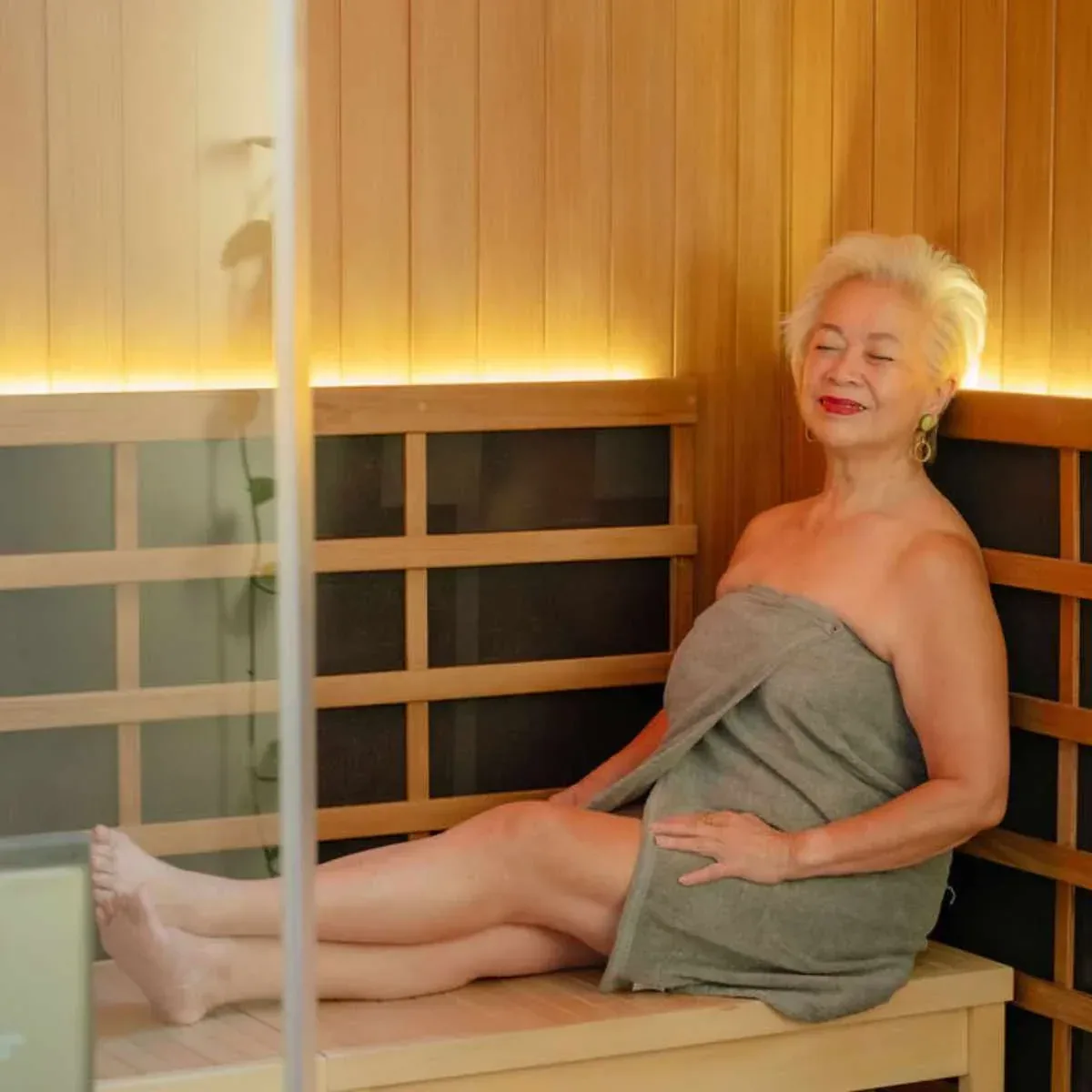 Woman wrapped in a towel sitting back in a bright wooden infrared sauna