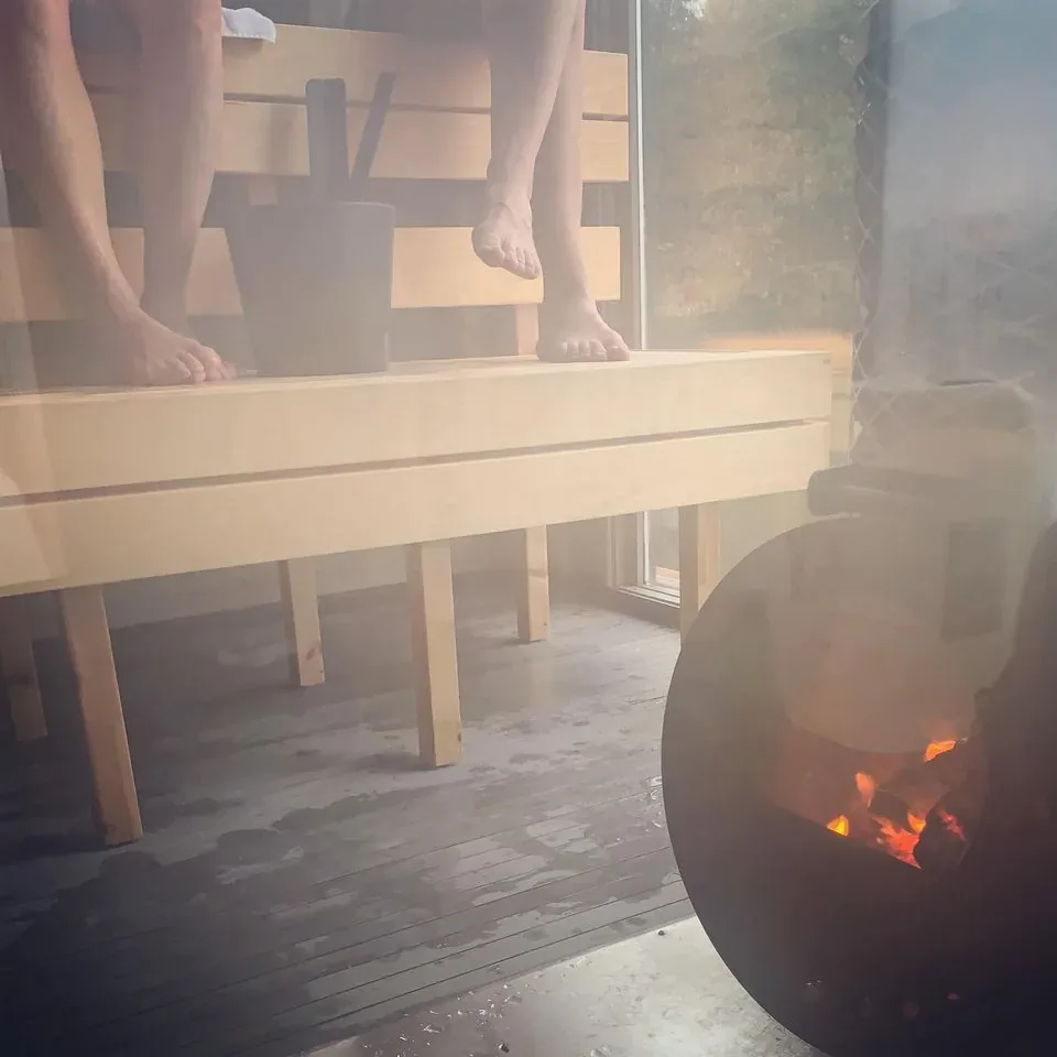 Feet on a wooden sauna bench next to a glowing wood stove