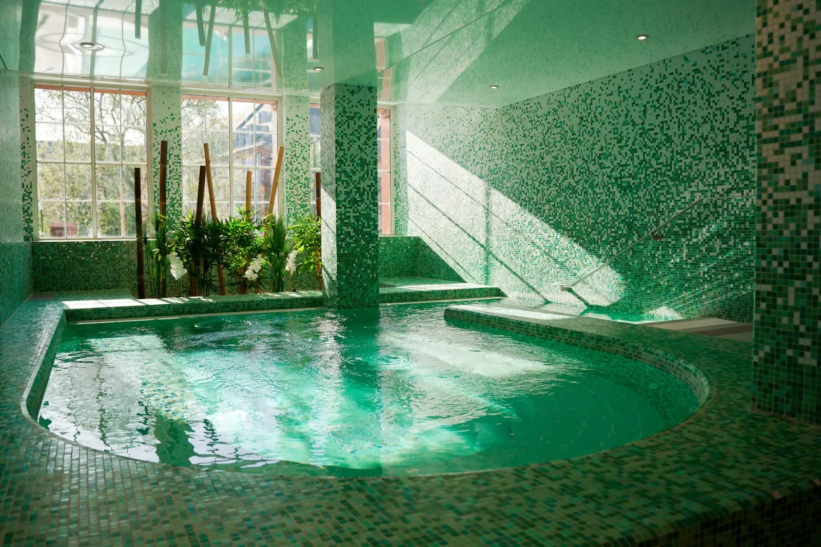 Green-tiled indoor pool with a window and plants, lit by sunlight