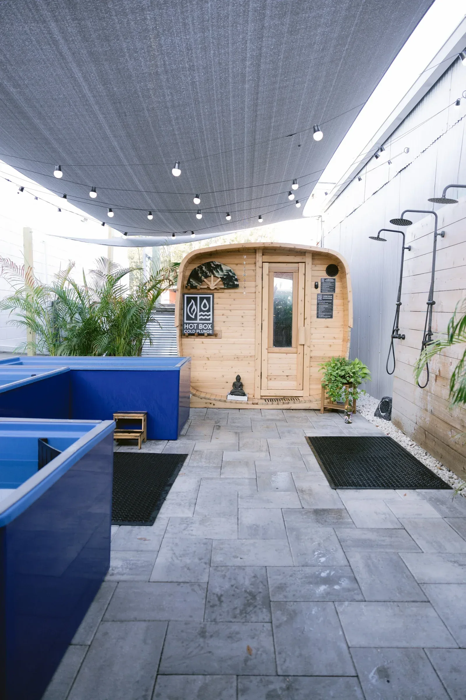 Outdoor courtyard with cold plunge tubs and showers in front of a small sauna