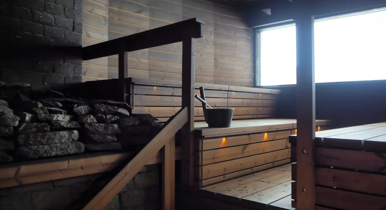 Tmavá dřevěná sauna se zčernalými stěnami a velkými kamennými kamny