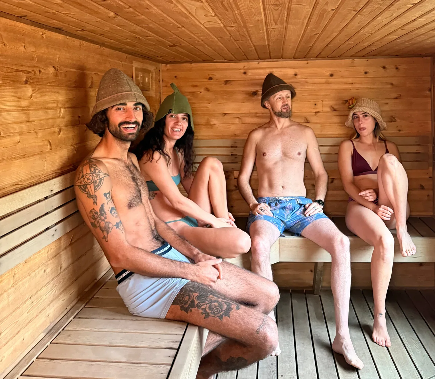 Four people in felt sauna hats sitting on wooden benches