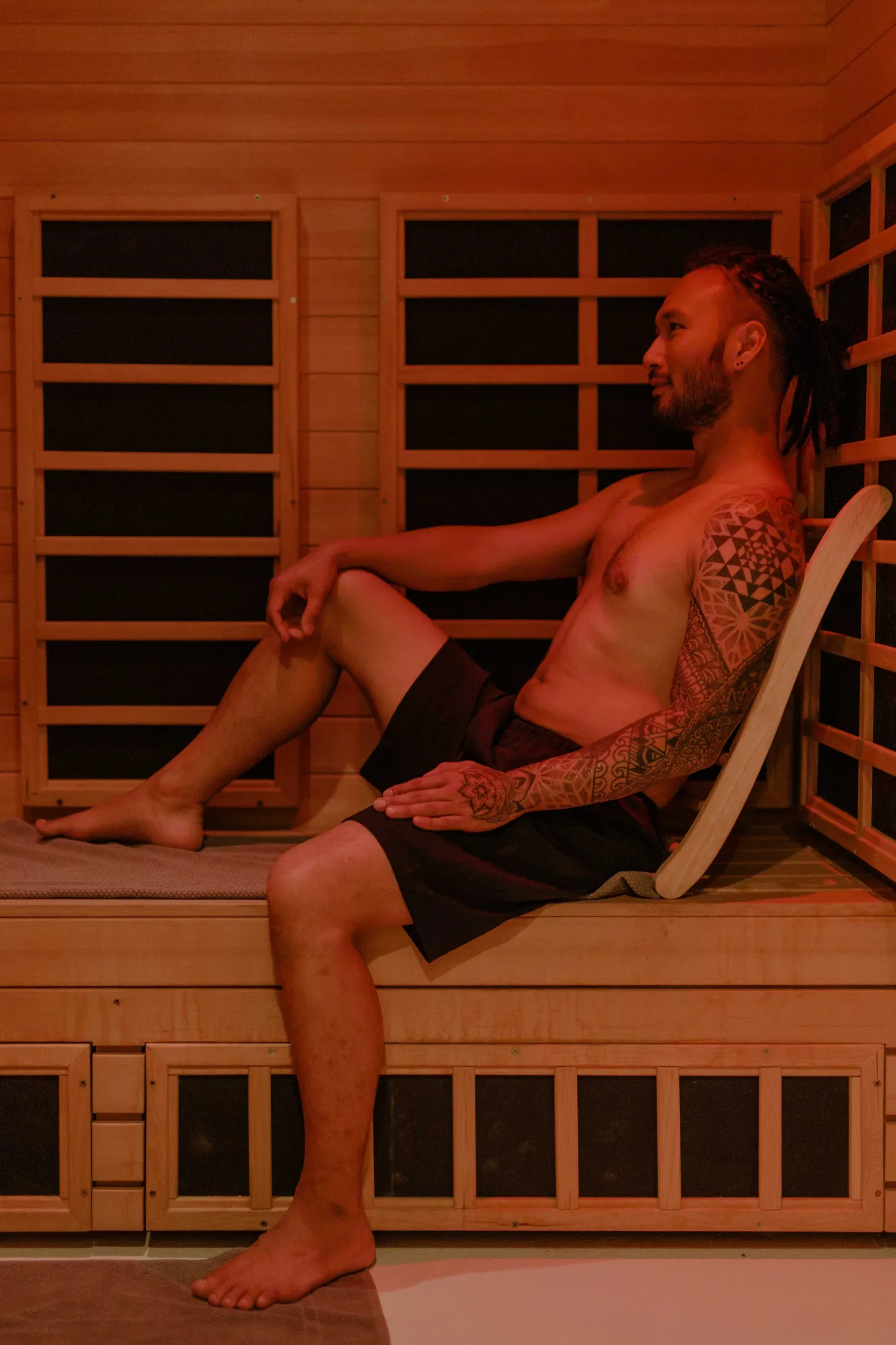 Man sitting in a wooden infrared sauna with dark heater panels on the walls around him