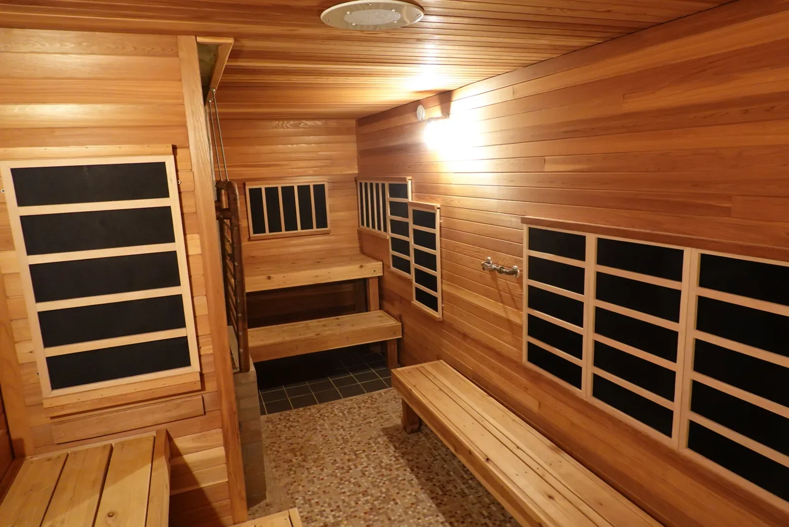 Wooden sauna room with rectangular dark infrared panels on two walls and a bench