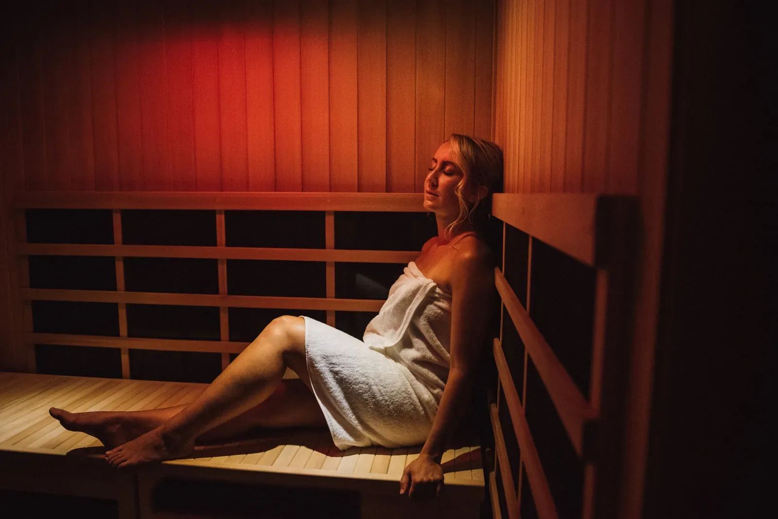 Woman in a towel relaxing in an infrared sauna with red light